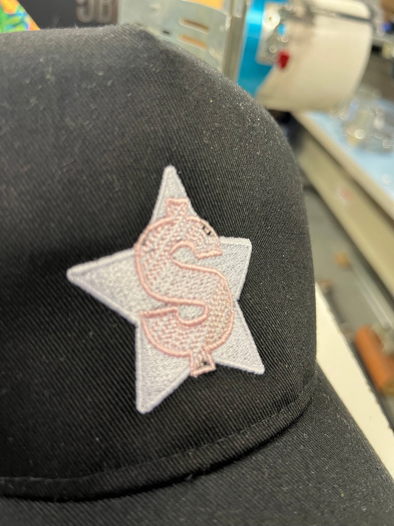translucent pink dollar sign stitched onto a hat with a solid white star on the background